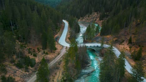 aerial flight above a scenic mountain river with fresh blue water in the bavarian austrian alps by afternoon sunshine, flowing down a riverbed along trees, forests, a street and hills seen by drone