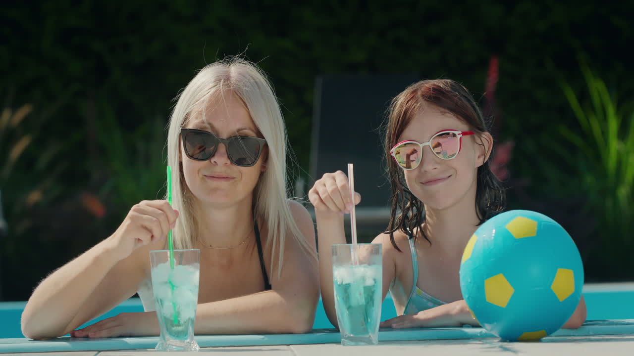 портрет матери с дочерью, расслабляющейся в бассейне. холодные напитки рядом с ними. смотрят в камеру