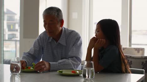 Front-view-of-cute-asian-granddaughter-and-old-grandfather-eating-food-a-dining-table-4k