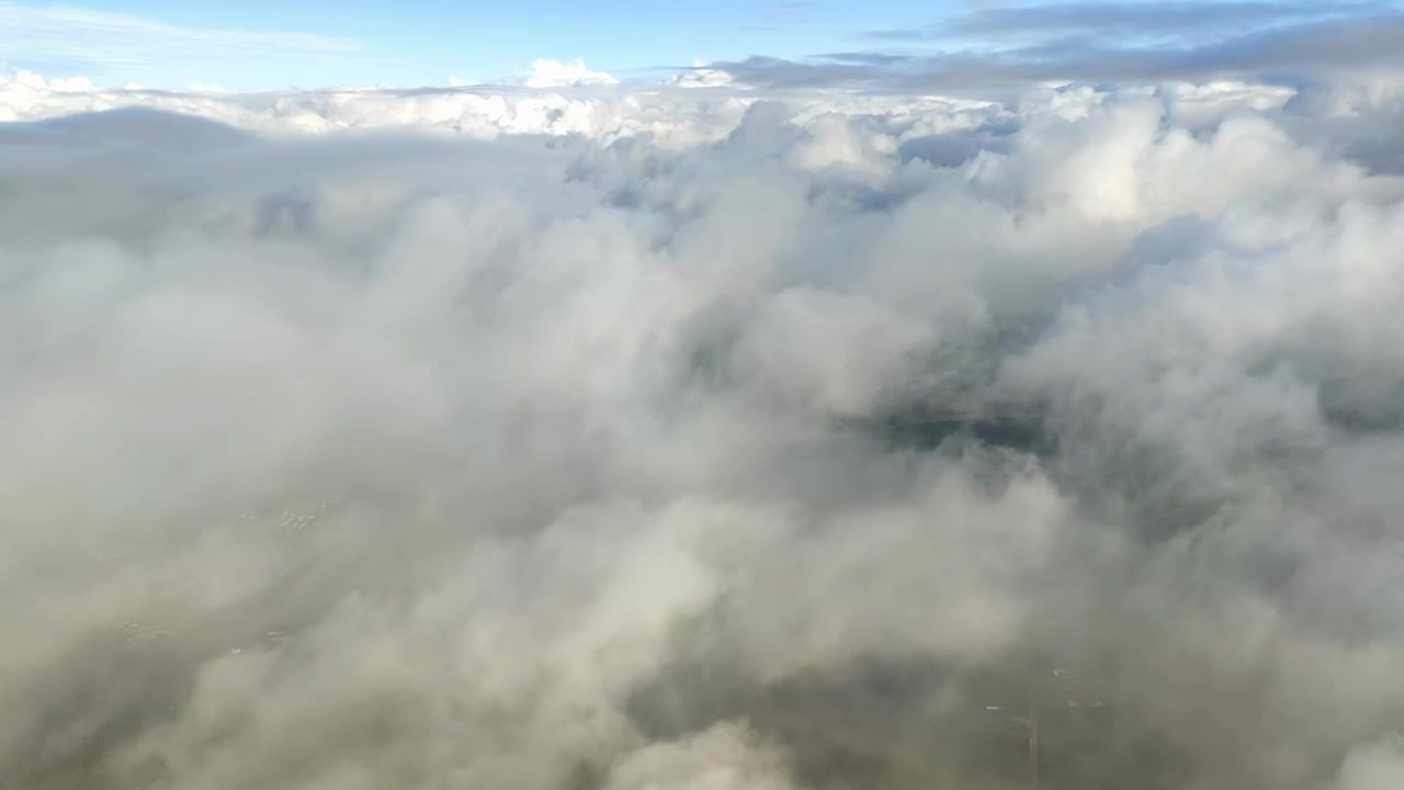 Avión desciende hacia las nubes con el suelo visible muy abajo. Termina cuando el avión entra en las nubes, la vista se vuelve blanca.