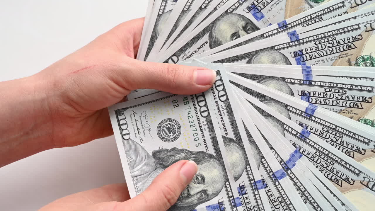Close up of female hands holding a wide fan of one hundred dollar bills