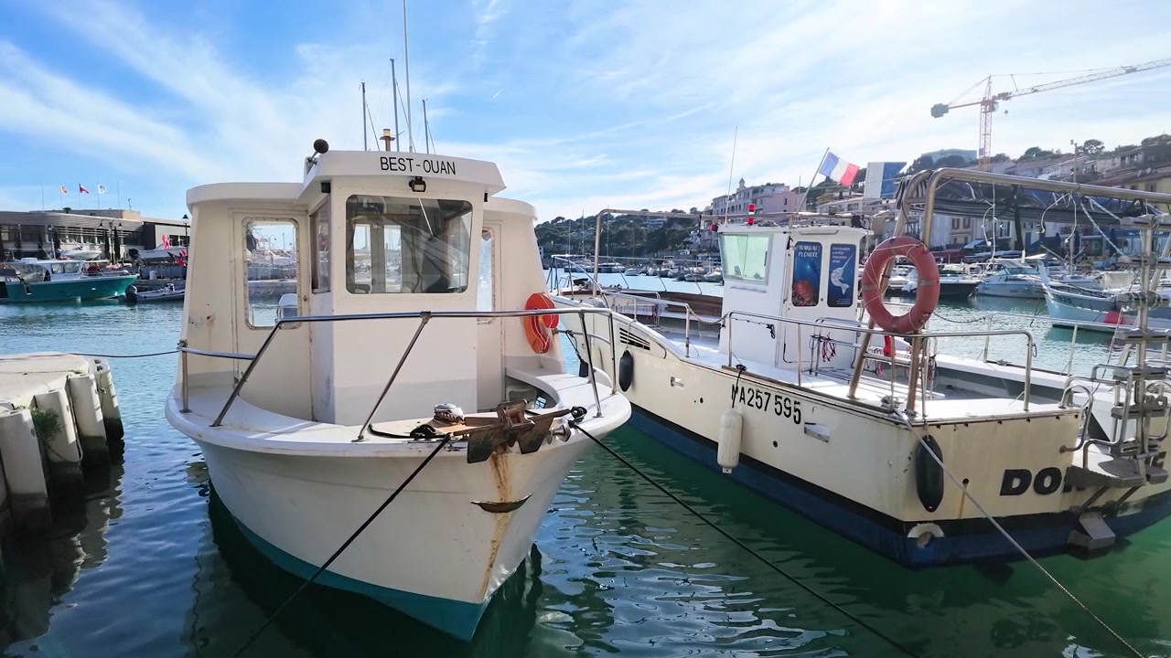 Inquadratura ampia e statica di barche da pesca bianche ormeggiate in un soleggiato porto mediterraneo a Cassis