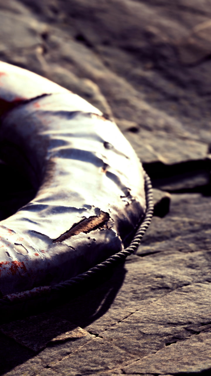 Lifebuoy resting on the rocky shoreline near water during daylight hours