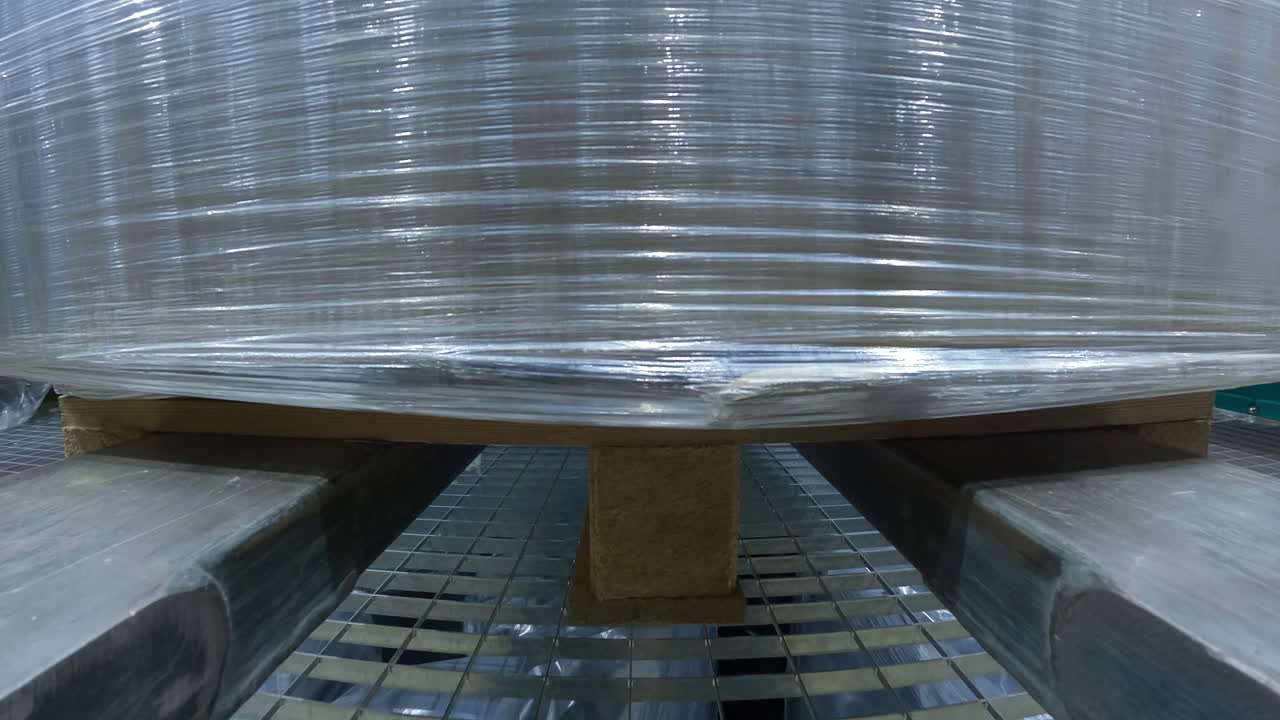 primer plano de un par de cuchillas que llevan una cubierta de carga de celofán de plástico, levantándola hacia abajo y convirtiéndose en la sala industrial del callejón