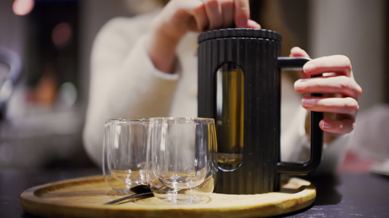 Mani che preparano tè caldo usando una moderna French press su un vassoio di legno con tazze di vetro