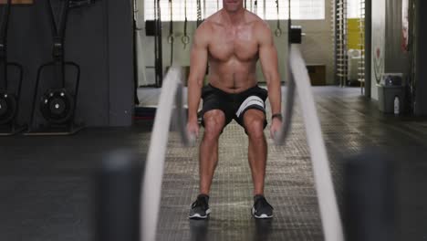 front view of an athletic caucasian man working out with battle ropes