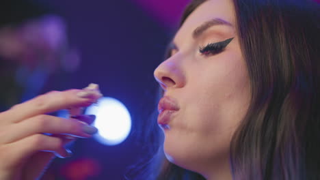close up of woman with long hair eating popcorn and gently adjusting strands while seated in studio environment with soft dim lighting in background