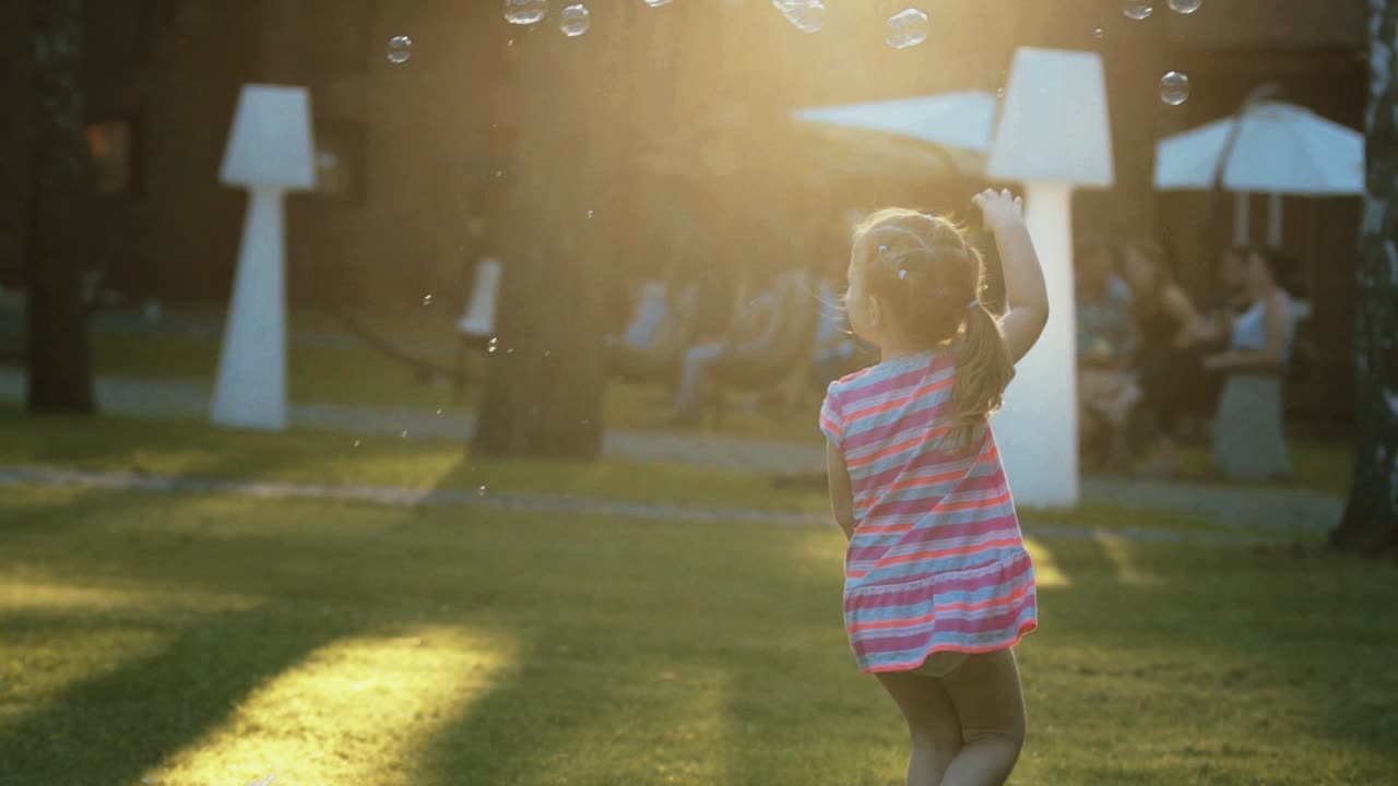 美しい小さな女の子がスローモーションで夕暮れの時に泡を捕まえる
