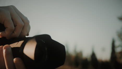 close-up of a focused male photographer with a mirrorless camera taking pictures out in nature at sunset