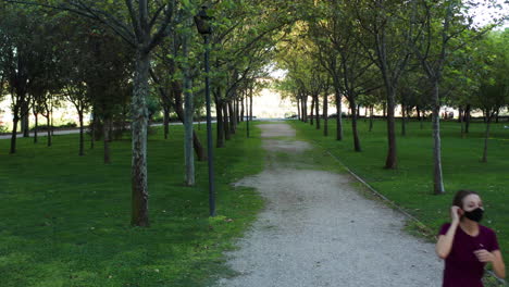 una mujer con una máscara tomando un descanso de trotar en el parque enrique tierno galván