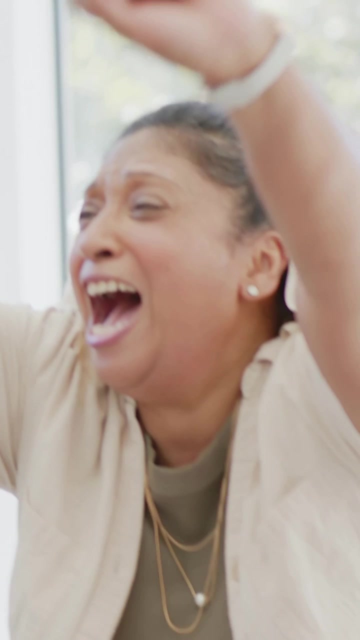 Vertical video: Reacting woman to offscreen cue raising arms on sofa in olive top while man smiling