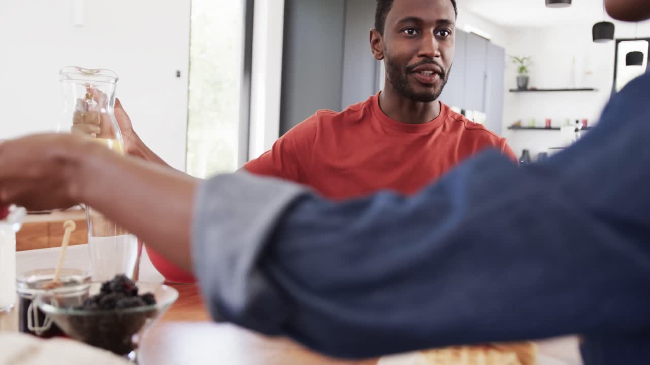 Happy african american couple pouring juice and serving breakfast at table in kitchen, slow motion