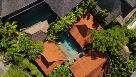aerial view capturing a tranquil setting, showcasing vibrant greenery, traditional balinese architecture, and a person swimming in the pool