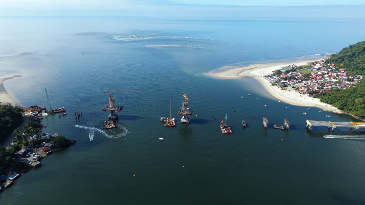 High altitude aerial panoramic movement over the new Guaratuba-Matinhos Bridge industrial facility and its concrete piles with cranes, Paraná, Brazil