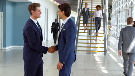 Two-Businessmen-Meet-In-Corridor-Of-Busy-Modern-Office