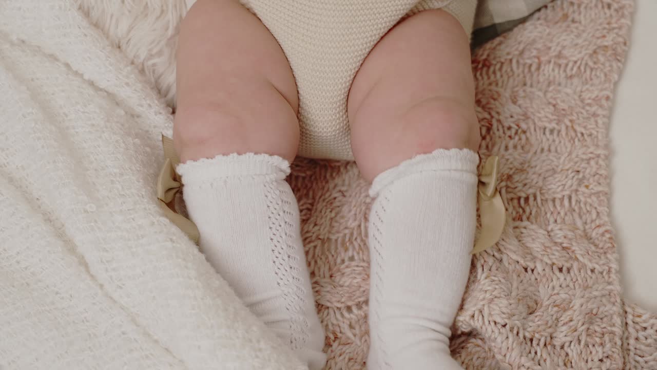 Gambe di neonato con calzini bianchi su una coperta lavorata a maglia, primo piano al rallentatore