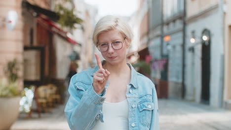 joven rubia molesta reaccionando a una idea desagradable y horrible sacudiendo el dedo a la cámara en la calle de la ciudad