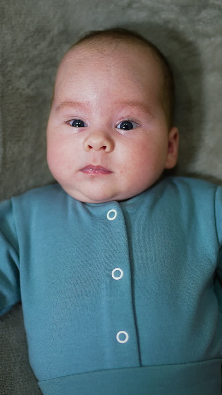 Baby boy wearing blue warm suit lying on the soft bed. Child moving his hands actively. Grey blanket background. Vertical video