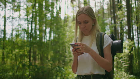 Attractive-woman-relax-in-forest-and-using-smartphone-outdoors.-Woman-Hiking-In-The-Forest-And-Typing-Message-On-Smartphone.-Solo-female-hiker-using-smart-phone.