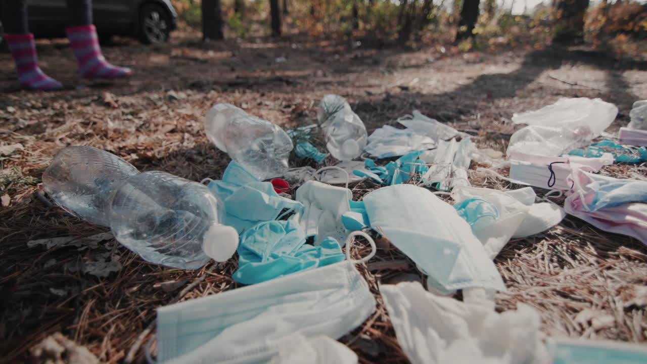 los pies del niño con botas caminan por el bosque pasando por un montón de basura