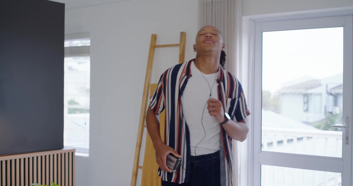 African American man pressing player, settling wired earphones, dancing to music by glass door