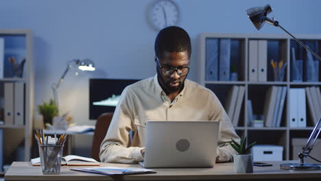 Office-Worker-Wearing-Glasses-And-Typing-On-The-Laptop-In-The-Office-At-Night