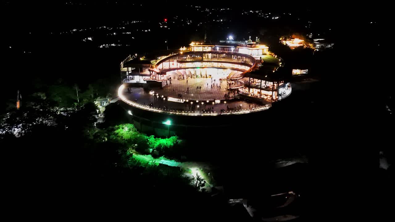 Vibrant night drone footage of a circular shopping and dining complex glowing with lights in the Philippines. Perfect for lifestyle, travel, and architecture projects