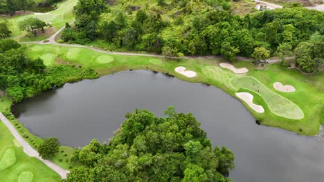 aerial footage captures a lush golf course in phuket, thailand, showcasing vibrant greens, sand bunkers, and serene water features