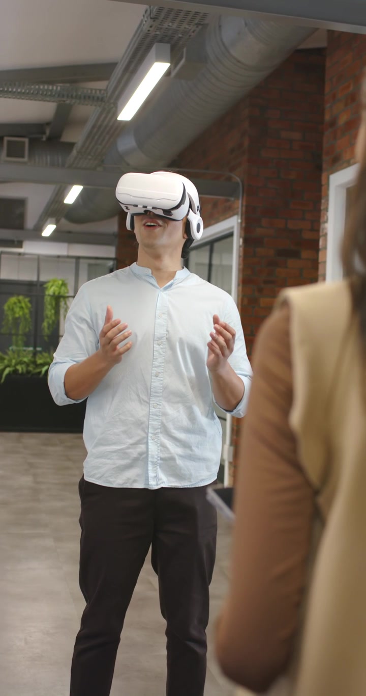 Video verticale: Team eterogeneo che guarda un uomo asiatico che indossa un visore VR e interagisce con un tablet in ufficio