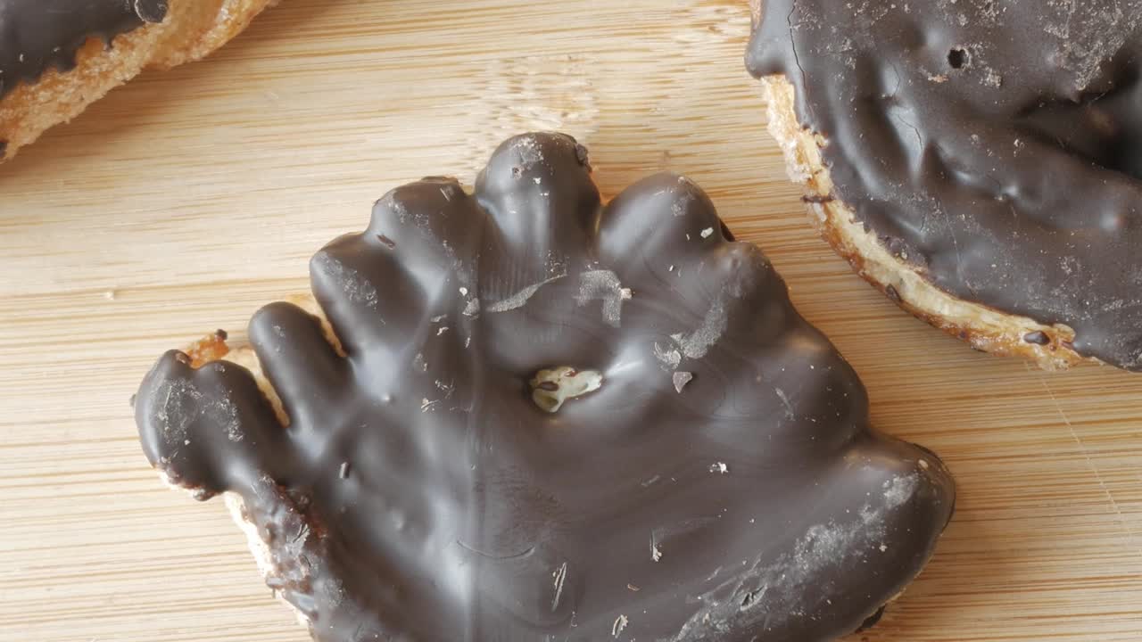A hand-shaped chocolate-covered palmera pastry, close-up shot on a wooden surface
