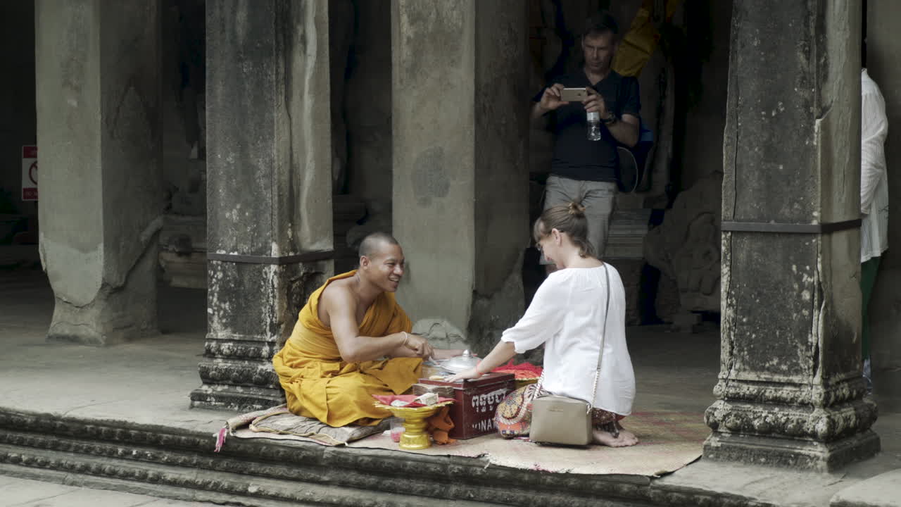 Female tourist got blessed by a buddhism monk in traditonal orange garb at the historical temple Angkor Wat.