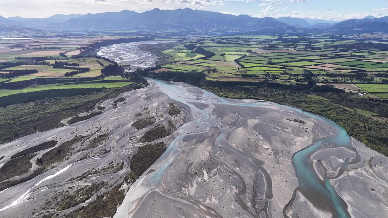 Vista aerea con drone di un fiume intrecciato che serpeggia attraverso l'Isola del Sud della Nuova Zelanda, rivelando canali intricati, letti di ghiaia e vasti paesaggi rurali.