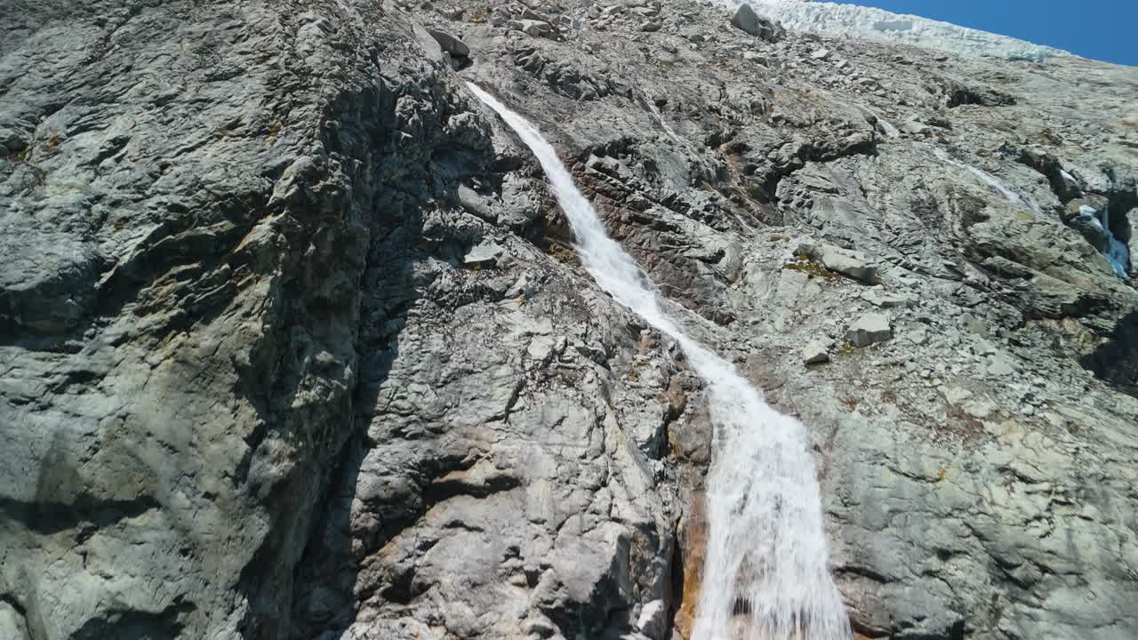 A spectacular aerial rising shot ascends alongside the glacier-fed waterfall cascading down Chacraraju into Laguna 69 in Peru