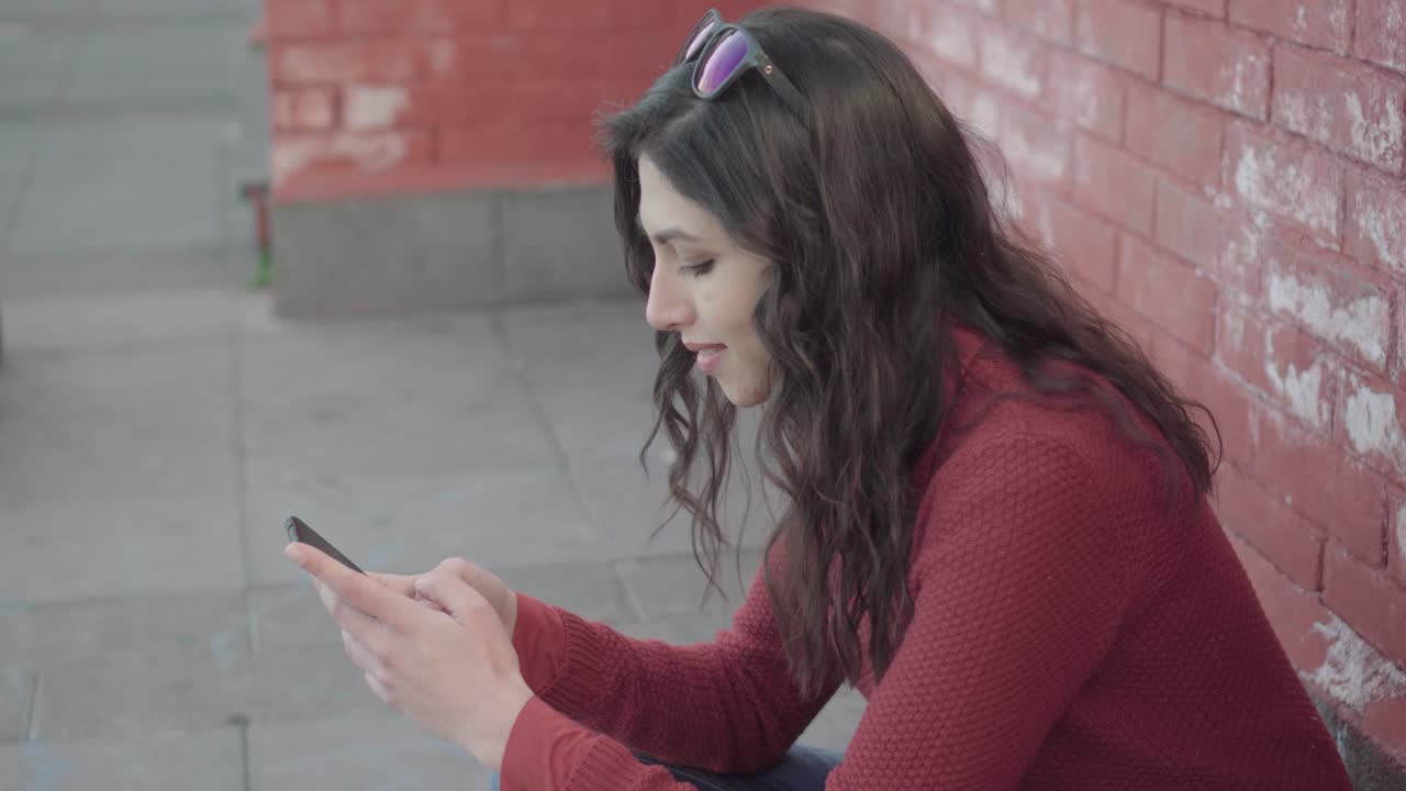 Ragazza che usa lo smartphone all'aperto vicino a un muro di mattoni, profilo statico