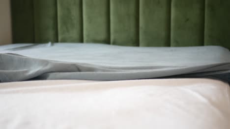 close up of a bed with green velvet headboard and gray sheets