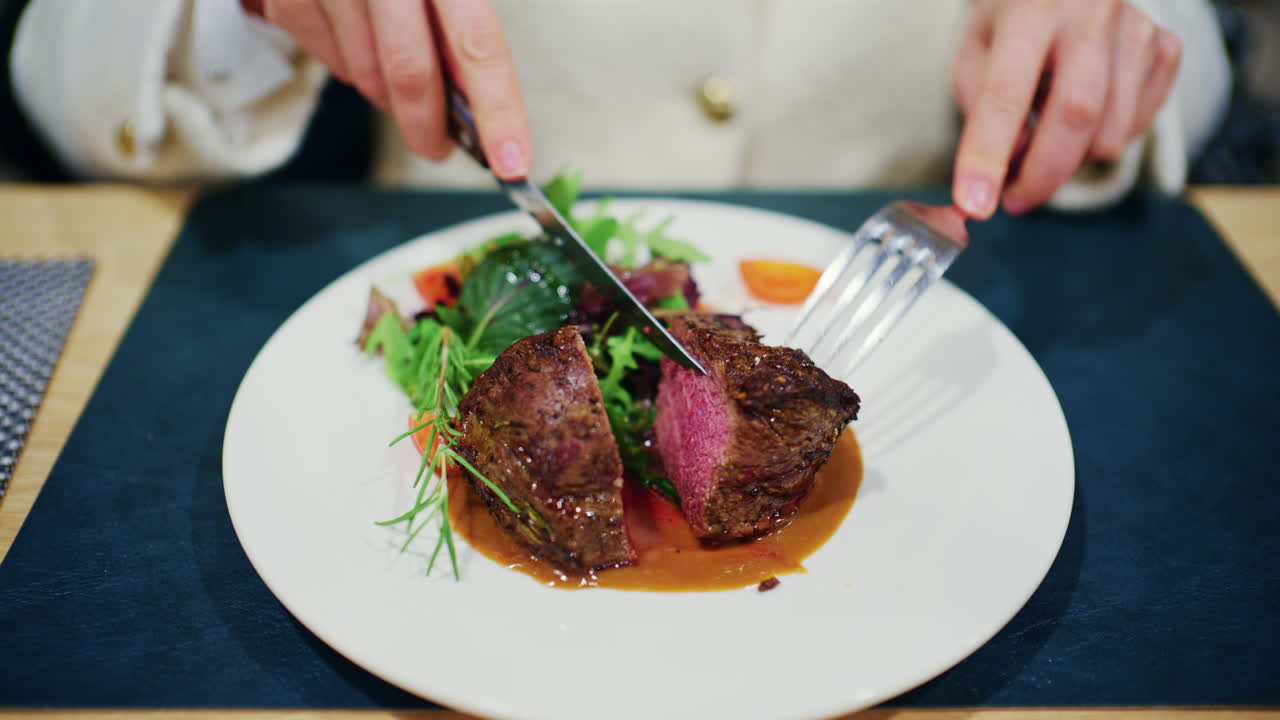 Donna che taglia una bistecca con cottura media al sangue servita con verdure e salsa su un piatto da ristorante