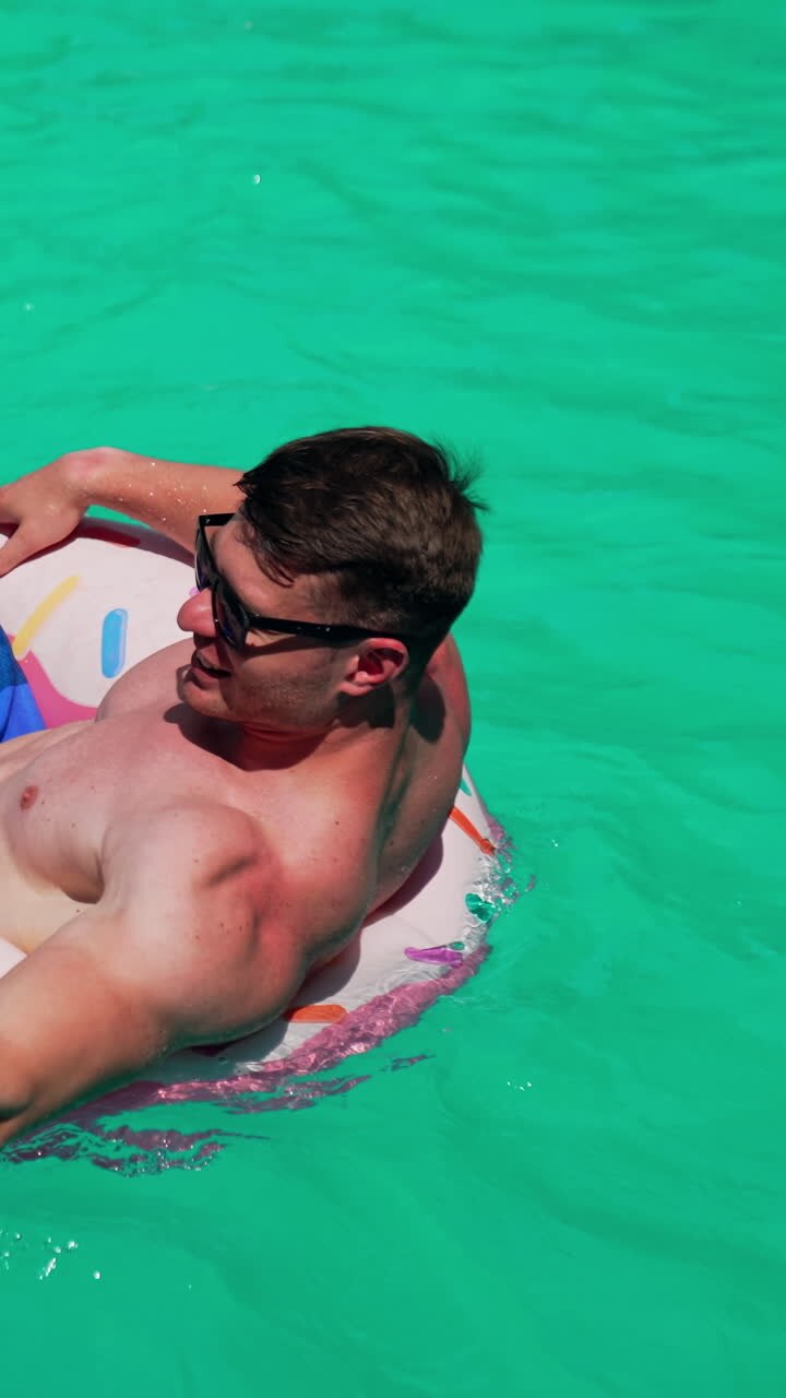 Man wearing sunglasses resting in the sun. Man sits in the inflatable circle in the pools rowing with hands. Vertical video