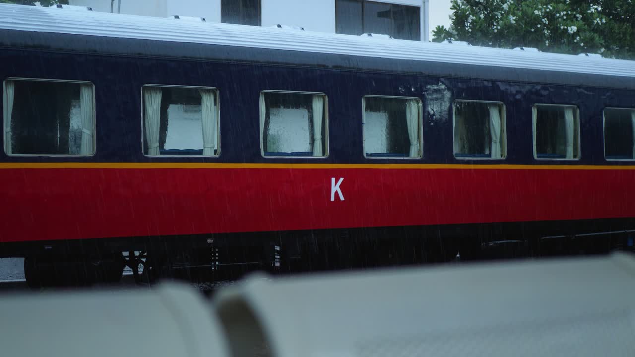 Heavy rain at a train station in Phnom Penh, with a close-up of a red and blue train car