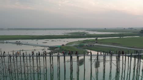 Asian-scenery-of-old-wooden-bridge-crossing-river-with-boats-looking-at-sunset