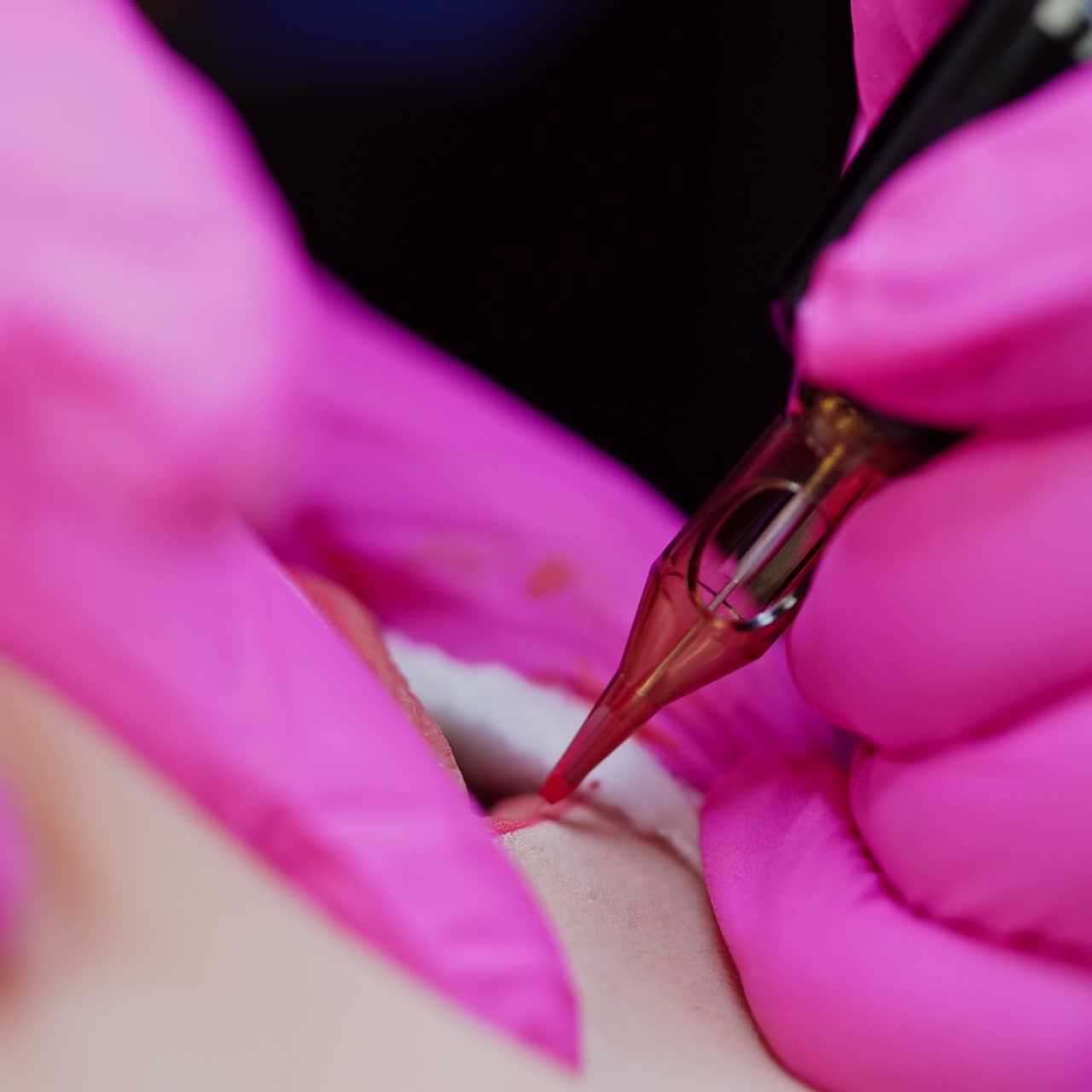 Applying red permanent makeup tattoo on lips. Tattooist in pink gloves making permanent make up on lips in beauty salon. Close-up.