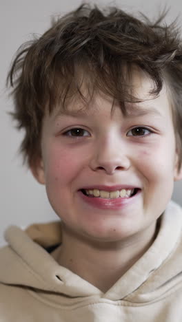 smiling brunet caucasian boy portrait. teenager in hoodie shows his teeth looking into camera. close up. vertical video