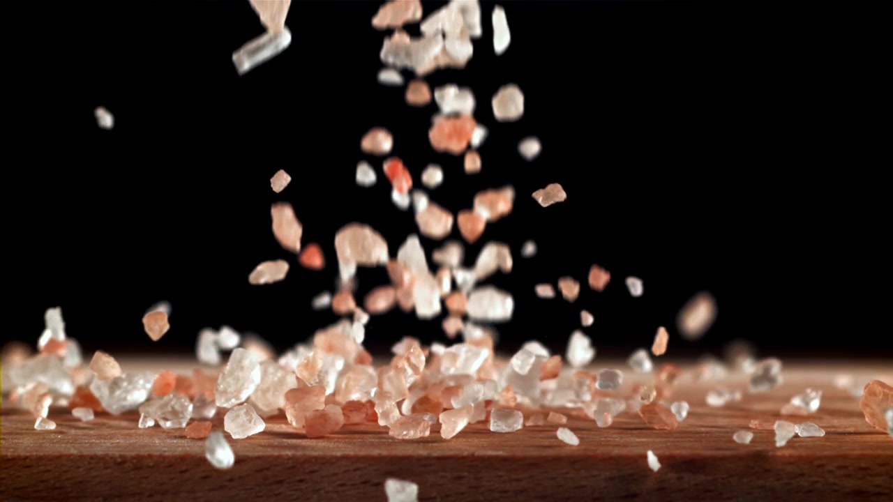 Himalayan Pink Salt Crystals Falling onto a Wooden Surface in Slow Motion