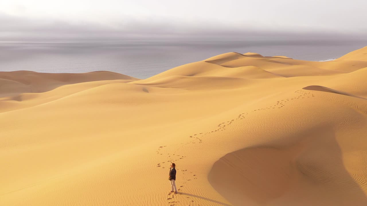 antena sobre una mujer modelo de pie en las hermosas dunas de arena del desierto de namib en namibia con el fondo de la costa de los esqueletos