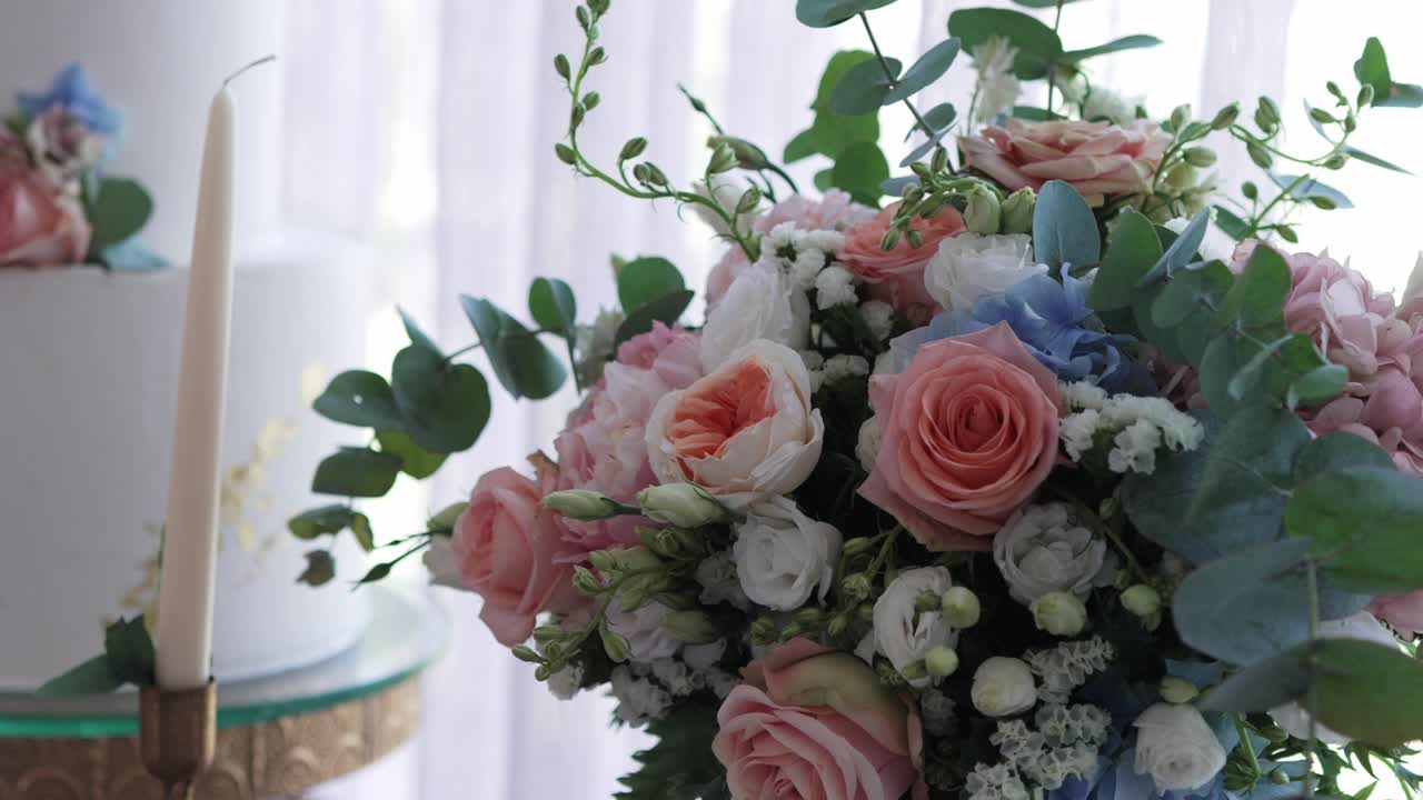 Close up of romantic wedding bouquet with roses beside elegant white cake and candlelight