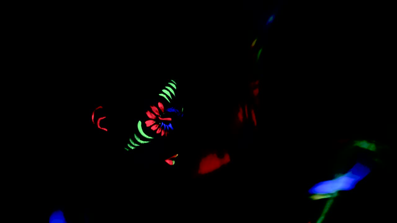 chica expresiva con pintura corporal ultravioleta de colores estirando los brazos y tocándose la cara