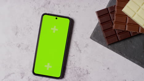 person putting down green screen mobile phone next to bars of milk plain and white chocolate