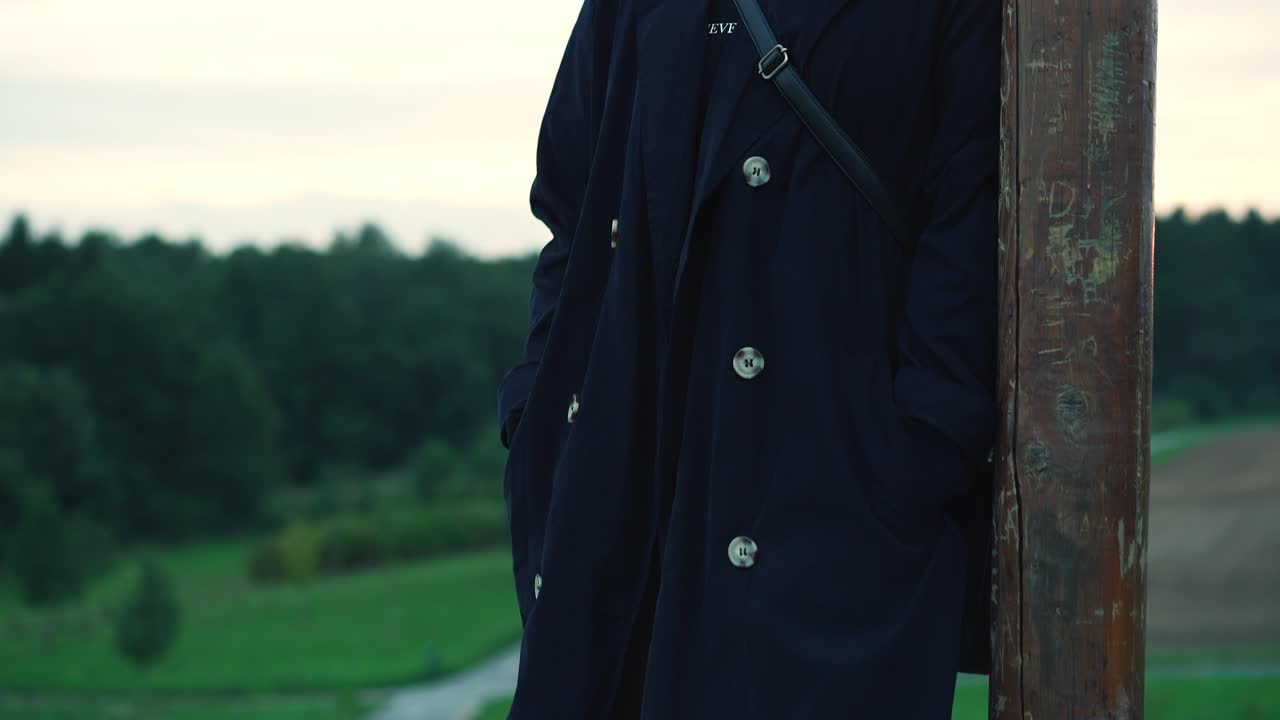 바람에 높은 곳에 서 있는 운동화와 함께 검은 긴 코트에 있는 소녀