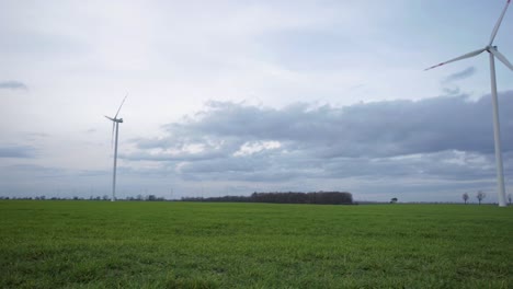 Panoramic-shot-of-a-windmill-farm,-in-a-country-field,-on-a-cloudy-and-windy-evening