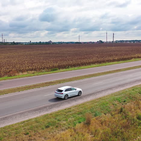 beautiful white car moving on the road. side view of new audi driving on highway on rural fields background under cloudy sky. aerial view.