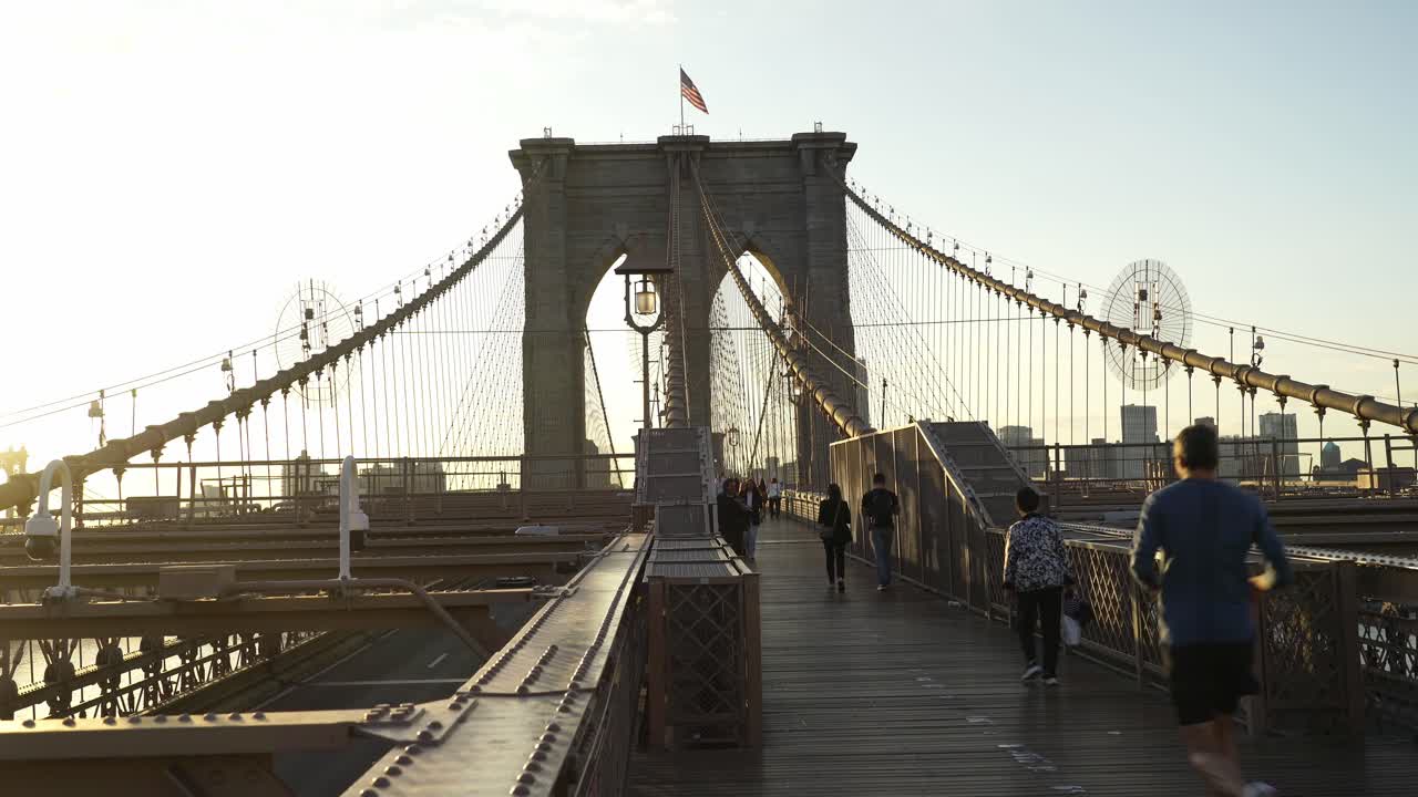 American Flag Waving on the Top of Brooklyn Bridge with People Walking Across It